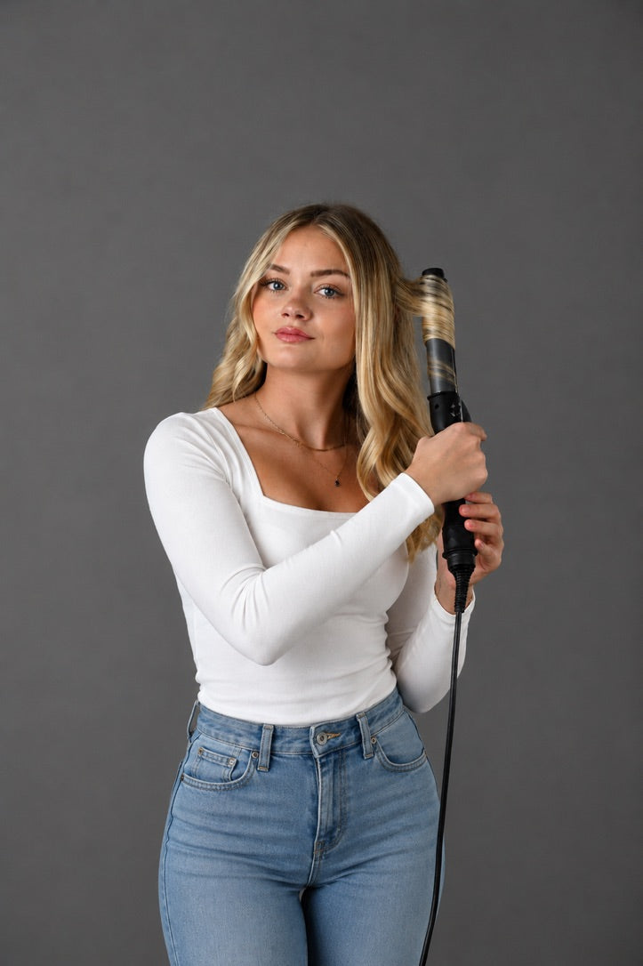 Woman holding a curling iron against a gray background